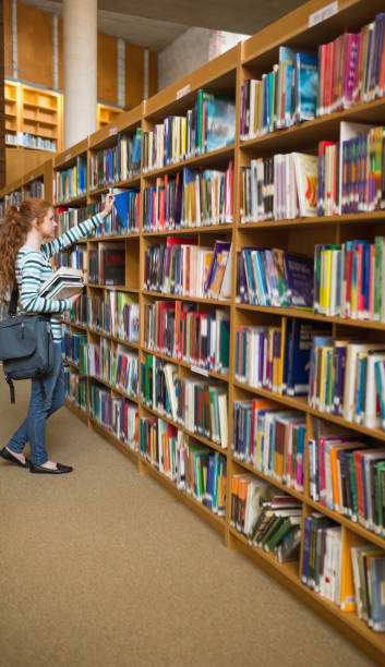 istock Redhead student taking a book from bookshelf in the library 837836240