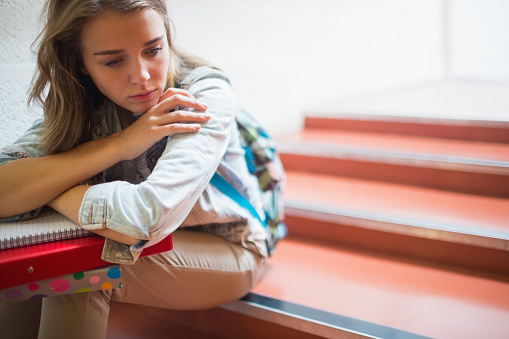 Sad lonely student sitting on stairs in college