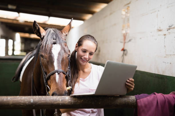 istock Smiling female jockey using laptop while standing by horse 837946228