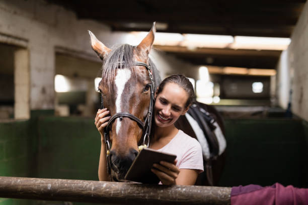istock Smiling female jockey using digital tablet while standing by horse 837946268
