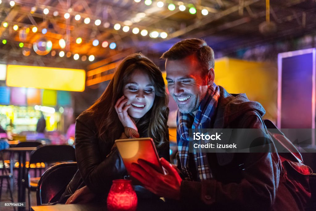 Couple at outdoor cafe with digital tablet Couple using digital tablet at a outdoor cafe. Caucasian man holding a digital tablet while sitting with his girlfriend at coffee shop in evening. Restaurant Stock Photo