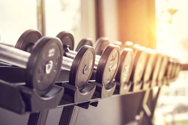 file di manubri in palestra con luce solare. - pesi da palestra foto e immagini stock