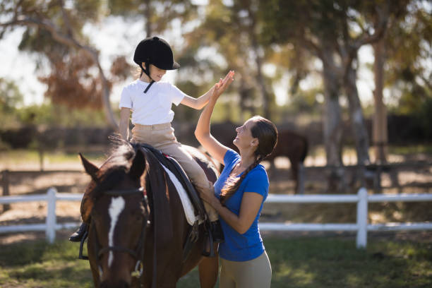Side view of woman giving high five to girl sitting on horse Side view of woman giving high five to girl sitting on horse in paddock all horse riding stock pictures, royalty-free photos & images