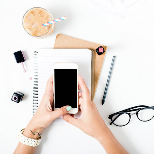 istock Feminine workspace with smartphone in female hands, latte ice, notebook, spectacles, nail polish and lipstick. Flat lay 837983194