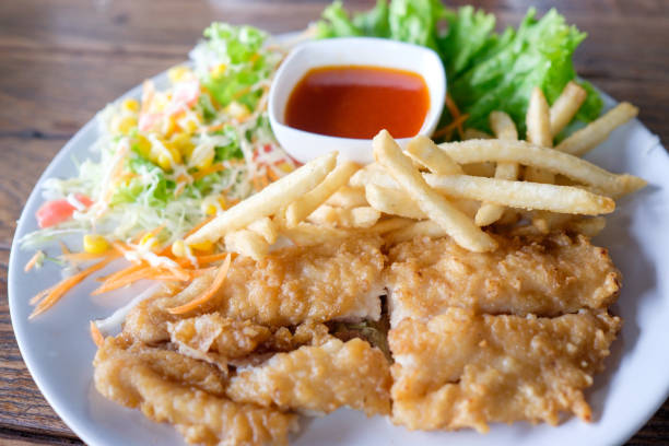 Fish dish - deep fried fish fillet and chips with vegetables on wooden background, Thai style Steak set on white round dish (Soft and Selective focus)