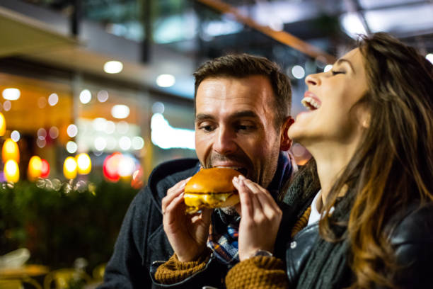 coppia felice che mangia fast food insieme - food people close up outdoors foto e immagini stock