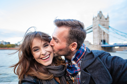 Mature man kissing his girlfriend outdoors. Romantic couple standing against tower bridge in london.