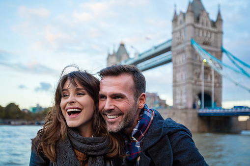 Smiling couple standing against tower bridge in london and looking away. Mature man and woman outdoors on a winter day.