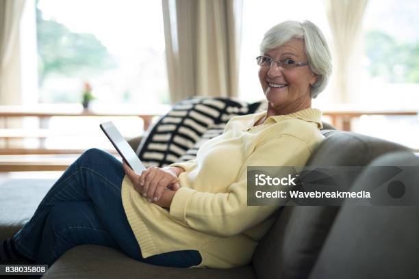 Smiling Senior Woman Using Digital Tablet On Sofa Stock Photo - Download Image Now - Cozy, Domestic Life, Senior Adult