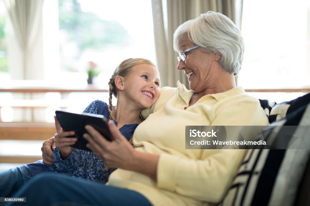 Smiling granddaughter and grandmother using digital tablet on sofa Smiling granddaughter and grandmother using digital tablet on sofa in living room Grandmother Stock Photo