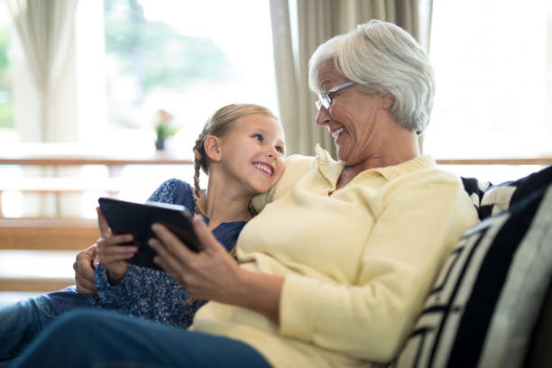 Smiling granddaughter and grandmother using digital tablet on sofa Smiling granddaughter and grandmother using digital tablet on sofa in living room granddaughter photos stock pictures, royalty-free photos & images