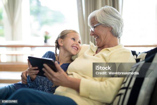 Smiling Granddaughter And Grandmother Using Digital Tablet On Sofa Stock Photo - Download Image Now