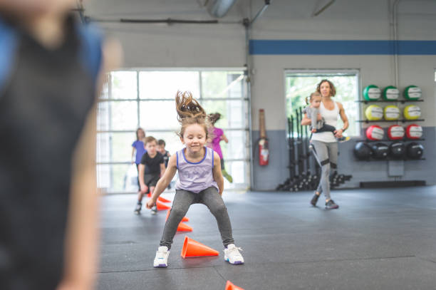 Never too young to start training A group of young children run through an obstacle course set up in the gym. They are all focused and having fun. A mom cheers them on. She is carrying a young child. community health center stock pictures, royalty-free photos & images