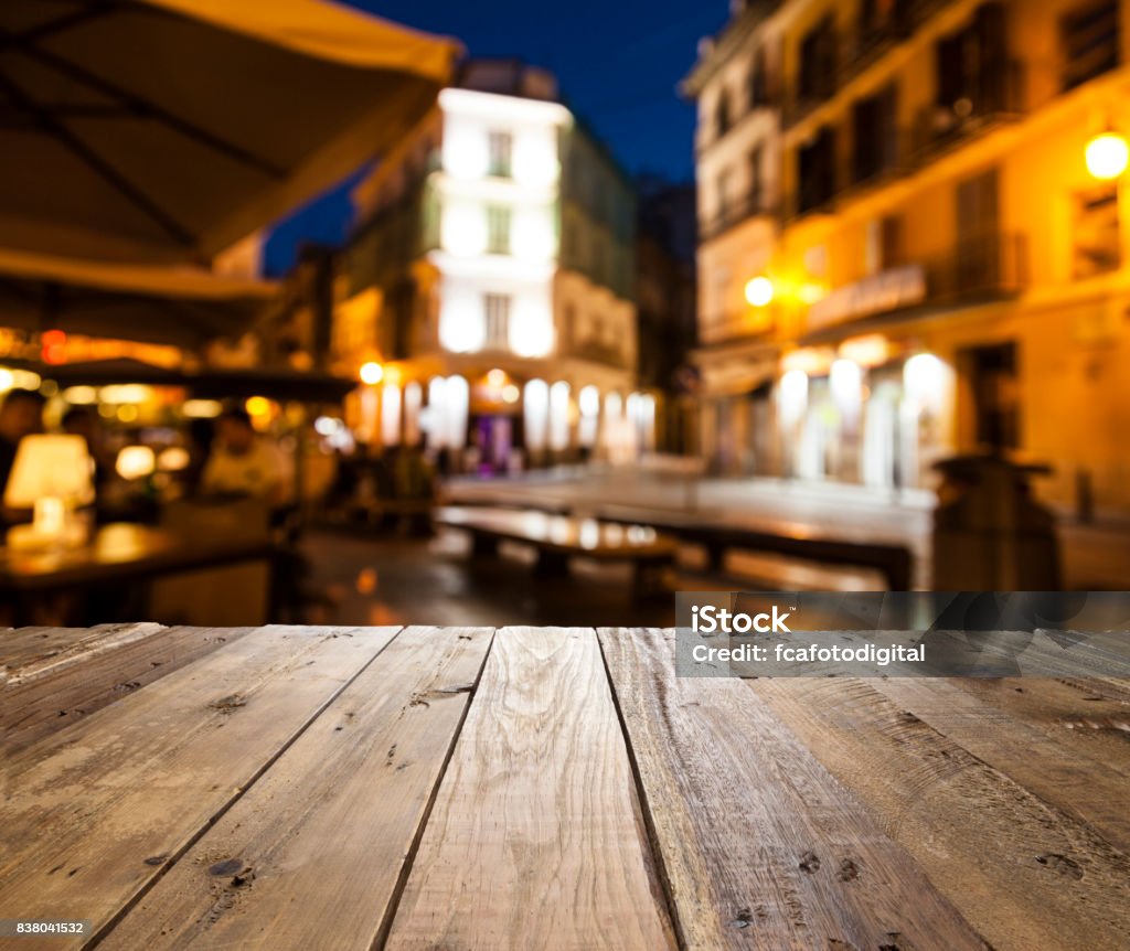 Empty wooden table with defocused street café at background Night view of an empty rustic wooden table in the foreground with defocused lights of a street café at background ideal for product or food display. Predominant colors are brown and yellow. DSRL outdoors photo taken with Canon EOS 5D Mk II and Canon EF 24-105mm f/4L IS USM Wide Angle Zoom Lens Abstract Stock Photo