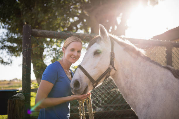 istock Smiling young woman standing by horse at barn 838055698