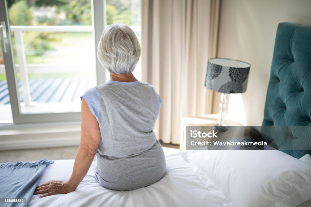 Senior woman sitting on bed in bedroom Rear view of senior woman sitting on bed in bedroom Bed - Furniture Stock Photo