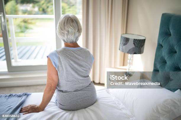 Senior Woman Sitting On Bed In Bedroom Stock Photo - Download Image Now - Bed - Furniture, Senior Adult, Senior Women
