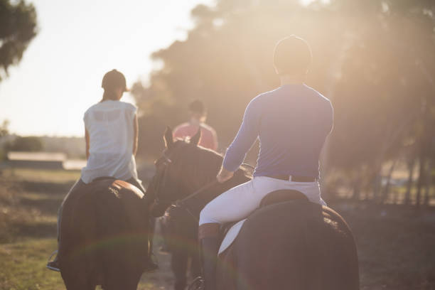 Rear view of trainer training women in riding horses at barn