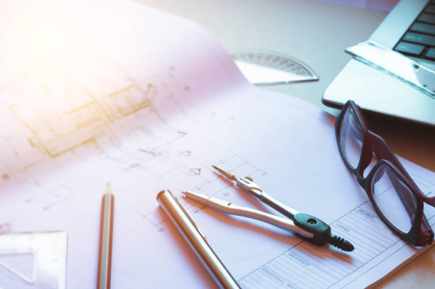 istock Table top view of Engineers table at office workplace.selective focus.Divider, pencil, pen, ruler, glasses and smartphone and blueprint on table top with window light. 838062366