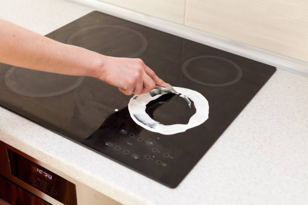 woman hands with bottle of cleaning detergent for induction stove applies a scour to the burner - stove ceramic burner electricity imagens e fotografias de stock