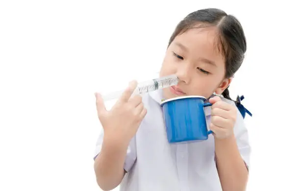 Nasal wash. asian student girl flushing her nose with syringe and saline isolated on white background