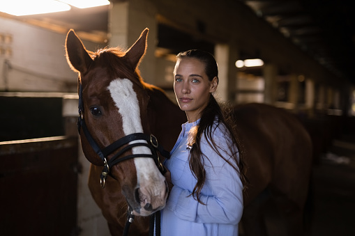 Portrait of confident female vet standing by horse in stable