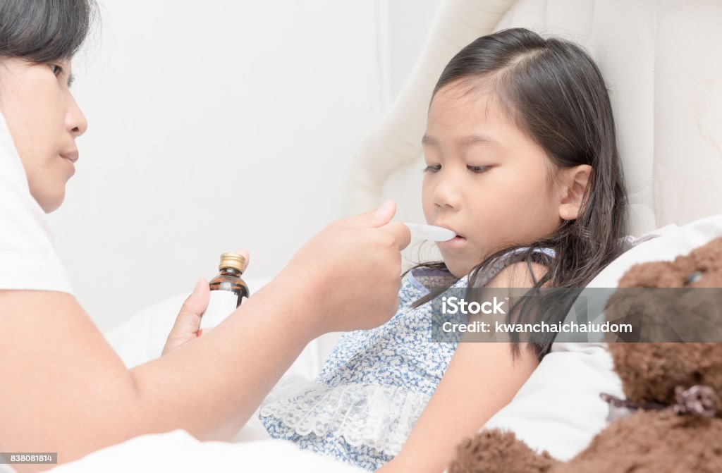Asian Mother giving her daughter  syrup because of the flu Asian Mother giving her daughter  syrup because of the flu in bedroom, sick child and health care concept Taking Medicine Stock Photo