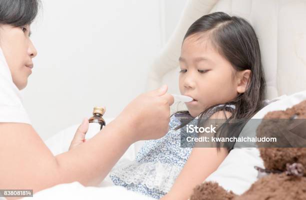 Asian Mother Giving Her Daughter Syrup Because Of The Flu Stock Photo - Download Image Now