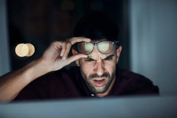 Shot of a young businessman looking angry while using a computer during a late night at work