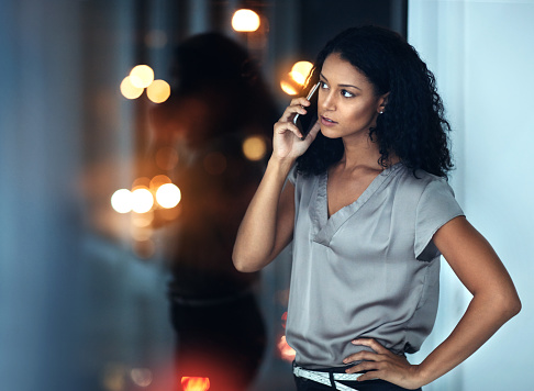 Shot of a young businesswoman talking on a mobile phone during a late night at work