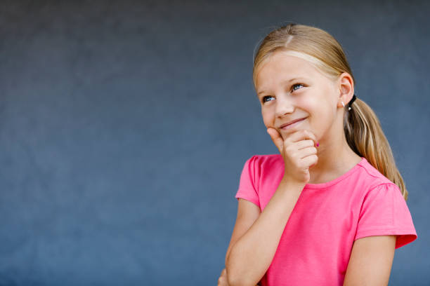 Thoughtful cover kid little lady posing at grey isolate backdrop, pensive looking up away. Portrait of girl child with ring on finger hand, studio shot. Youth image trends concept. Copy ad text space