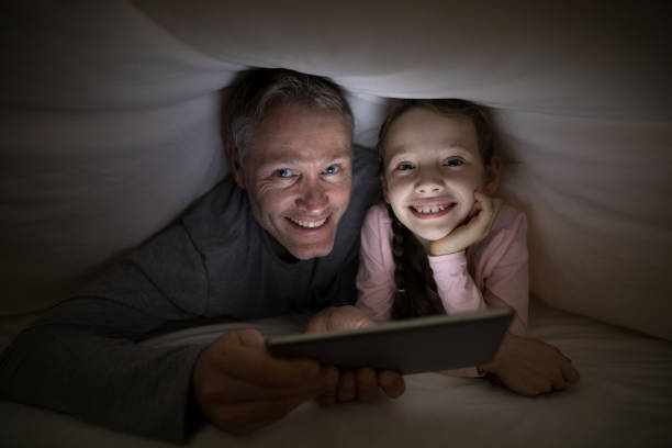 istock Smiling father and daughter with digital tablet under blanket on bed 838109990