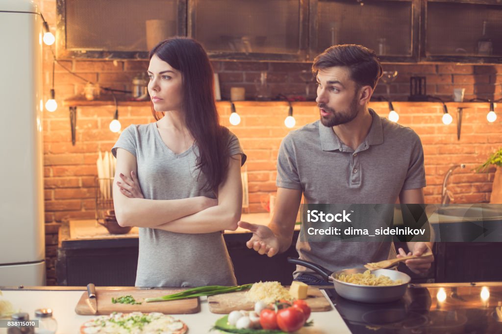 Young couple cooking in kitchen Young beautiful couple in kitchen. Family of two quarrelling while preparing food. Nice loft interior with light bulbs Couple - Relationship Stock Photo