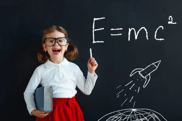 Child girl prodigy student with book near school blackboard