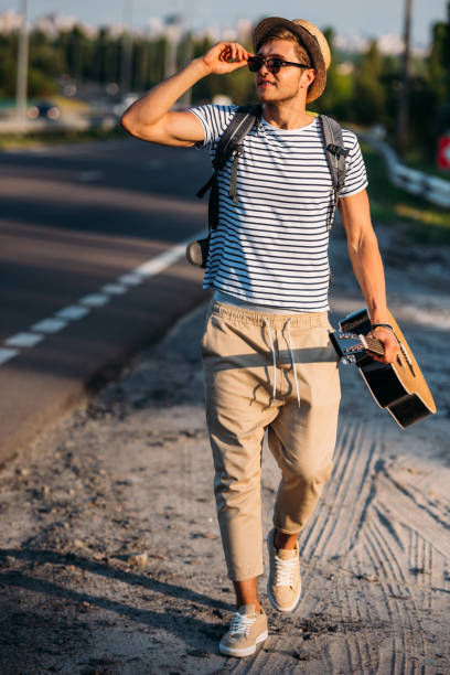 istock young man with guitar walking along road while hitchhiking alone 838139686