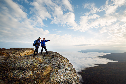 Two climbers standing on top of summit above clouds in the mountains. Man pointing with his hand discussing route. Plan, vision and mission concept.