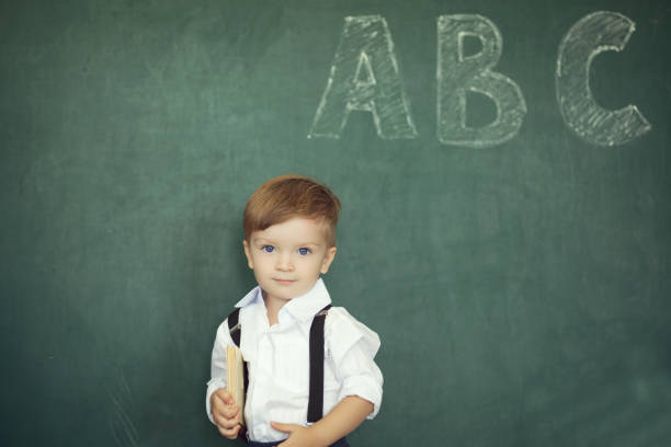 istock Cheerful smiling boy with books on a green chalkboard background 838195160