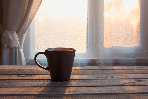 Cup of black coffee and a lace in front of the window on the wooden background.