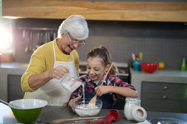 istock Grandmother adding water while granddaughter is mixing flour in a bowl 838218378
