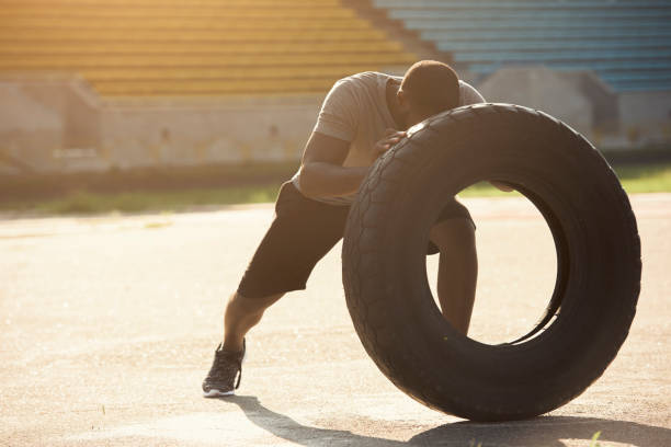 An athletic black man is performing tractor tire exercizes, flipping it
