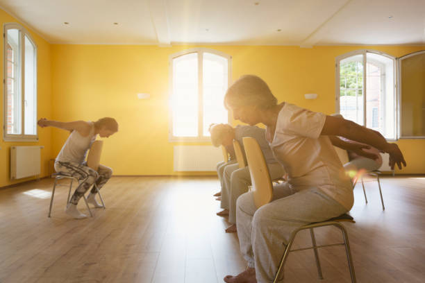 Teacher and active senior women doing yoga class on chairs