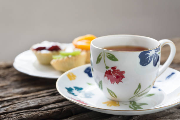 A porcelain cup of tea and delicious fruit tarts on the wood table