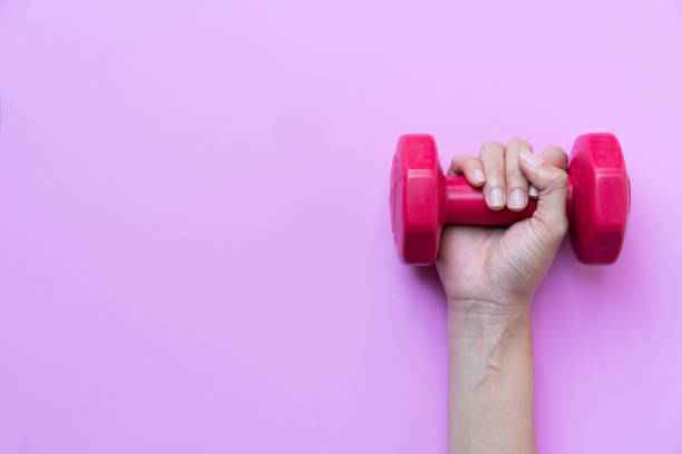 istock woman hand holding red dumbbell on pink background 838267302