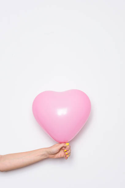 istock Pink heart baloon in hand on white wall 838268558