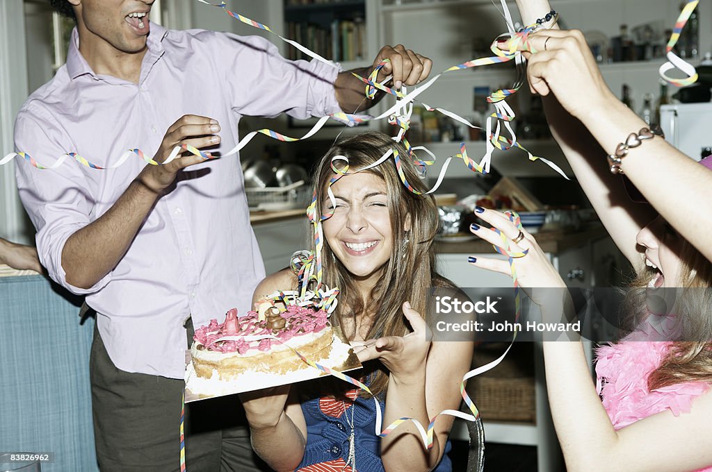 Friends throwing streamers over woman holding cake  Birthday Stock Photo