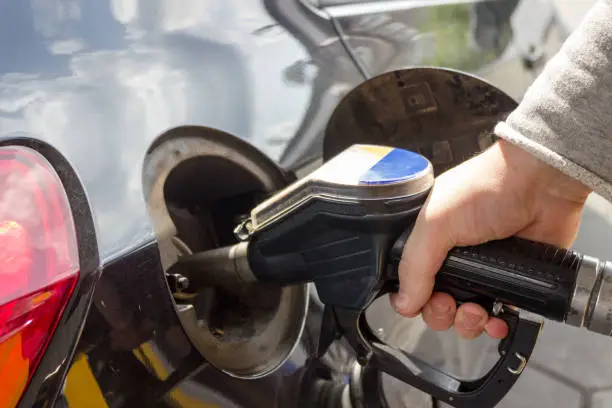 Close-up of hand refueling car's tank by holding petrol pump nozzle.