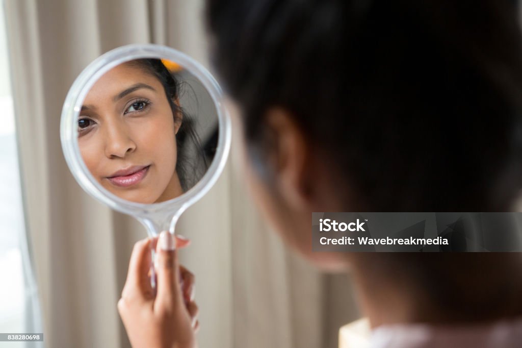 Woman reflecting on hand mirror Young woman reflecting on hand mirror at home Mirror - Object Stock Photo