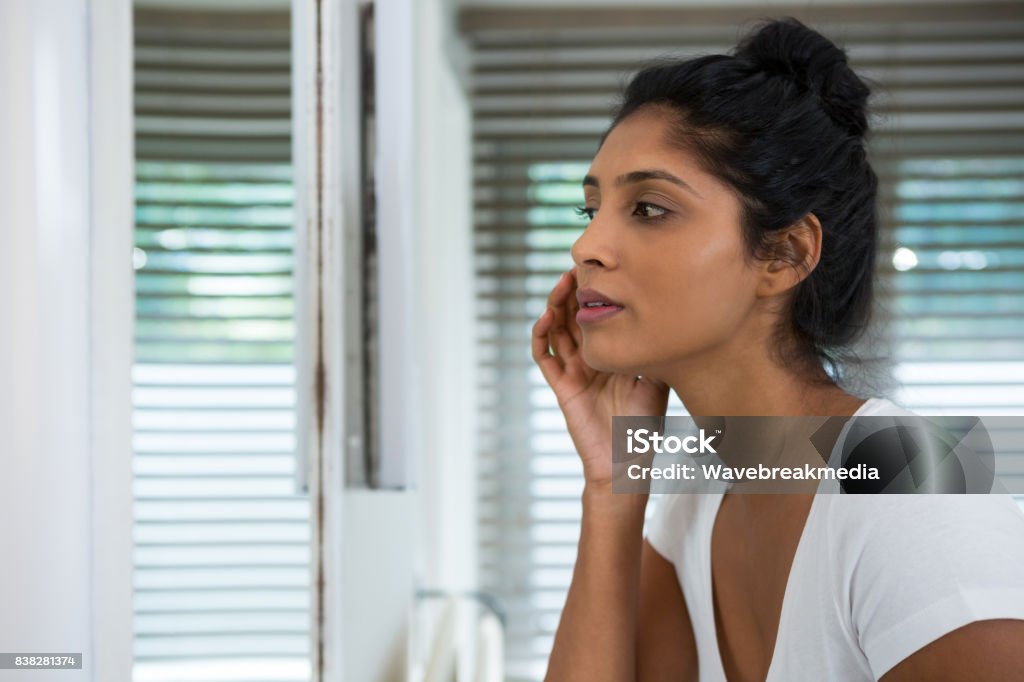 Woman touching face in bathroom Woman touching face looking into mirror in bathroom at home Acne Stock Photo