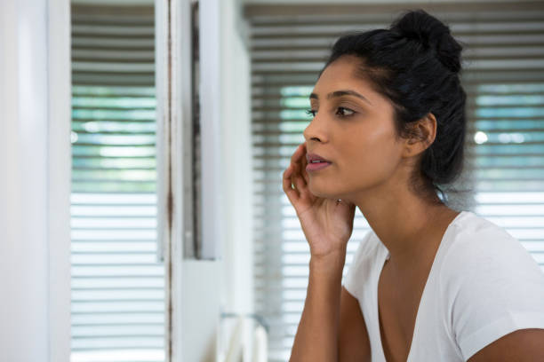 Woman touching face in bathroom Woman touching face looking into mirror in bathroom at home looking in mirror stock pictures, royalty-free photos & images