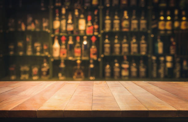 tavolo in legno con bancone sfocato e bottiglie sfondo - beer bar counter bar drink foto e immagini stock